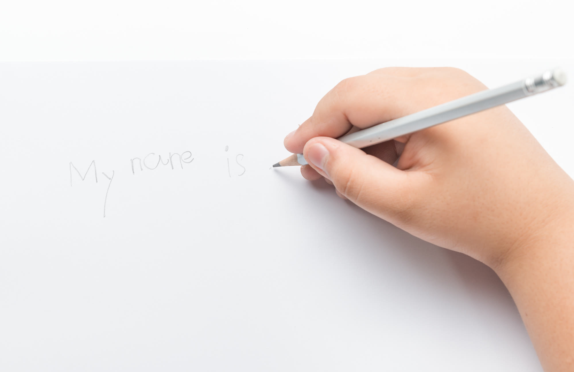 A child’s hand writing “My name is” in pencil
